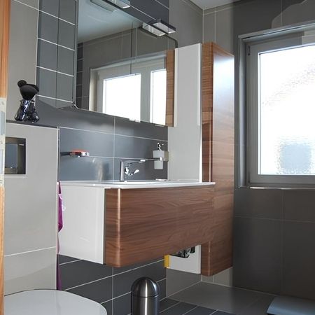 Badezimmer mit dunkelgrauen Fliesen und Schrankfronten in Holzoptik